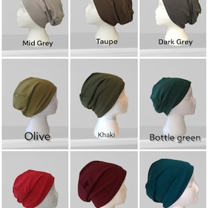 May include: A collection of nine solid-colored beanies displayed on mannequin heads. Colors include mid-grey, taupe, dark grey, olive, khaki, bottle green, red, bordeaux, and petrol. Each beanie is a different shade.