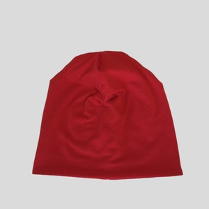 May include: A solid red beanie hat made of soft fabric. The hat is a deep, vibrant red color and appears to be folded at the top. The beanie is likely designed for warmth and casual wear.