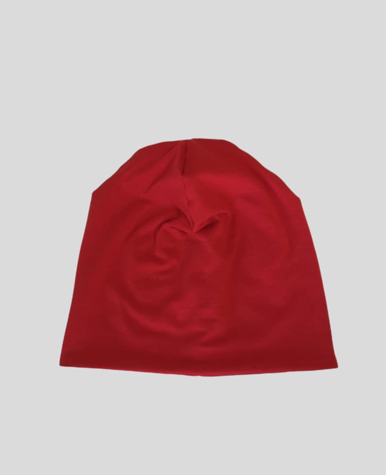 May include: A solid red beanie hat made of soft fabric. The hat is a deep, vibrant red color and appears to be folded at the top. The beanie is likely designed for warmth and casual wear.