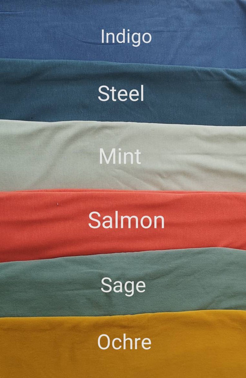 May include: A fabric swatch display featuring six different colors: Indigo, Steel, Mint, Salmon, Sage, and Ochre. Each color is labeled with its name in white text. The fabric appears to be a soft, solid material.
