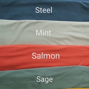 May include: A fabric swatch display featuring six different colors: Indigo, Steel, Mint, Salmon, Sage, and Ochre. Each color is labeled with its name in white text. The fabric appears to be a soft, solid material.
