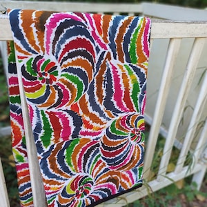 Peut inclure: Un tissu coloré avec un motif en spirale dans des tons de rose, rouge, orange, jaune, vert, bleu et marron. Le tissu a un fond blanc et une bordure noire.