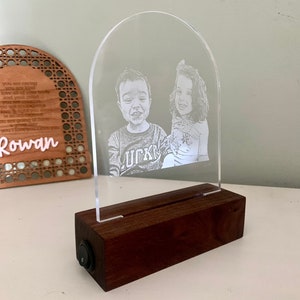 May include: A clear acrylic night light with a wooden base. The light features an engraved image of two children. The base has a switch to turn the light on and off.