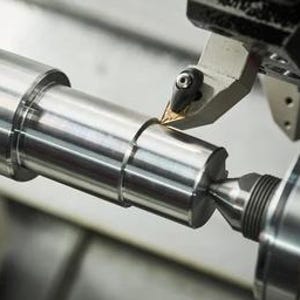 Puede incluir: Primer plano de una barra de metal que se está mecanizando en un torno. La herramienta de corte es visible y las virutas de metal salen volando de la barra.