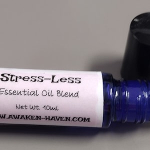 May include: A blue and white roller bottle with a black cap. The label reads "Stress-Less Essential Oil Blend" and "Net wt. 10ml" with the website "www.awaken-haven.com".