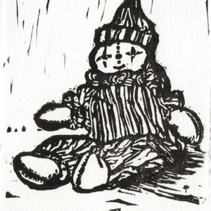 May include: Black and white linocut print of a clown doll wearing a striped hat and outfit. The doll is sitting with its legs crossed and has a simple, smiling face. The print is signed "Patch" and dated "22/30".