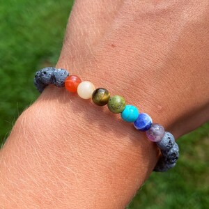 May include: A bracelet made of black lava rock beads and colorful gemstone beads. The beads are arranged in a rainbow pattern, starting with red, orange, yellow, green, blue, indigo, and violet.