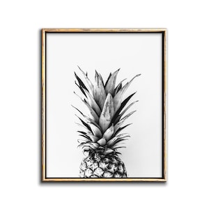 May include: A black and white photograph of a pineapple with a gold frame. The pineapple is centered in the image and the background is white.