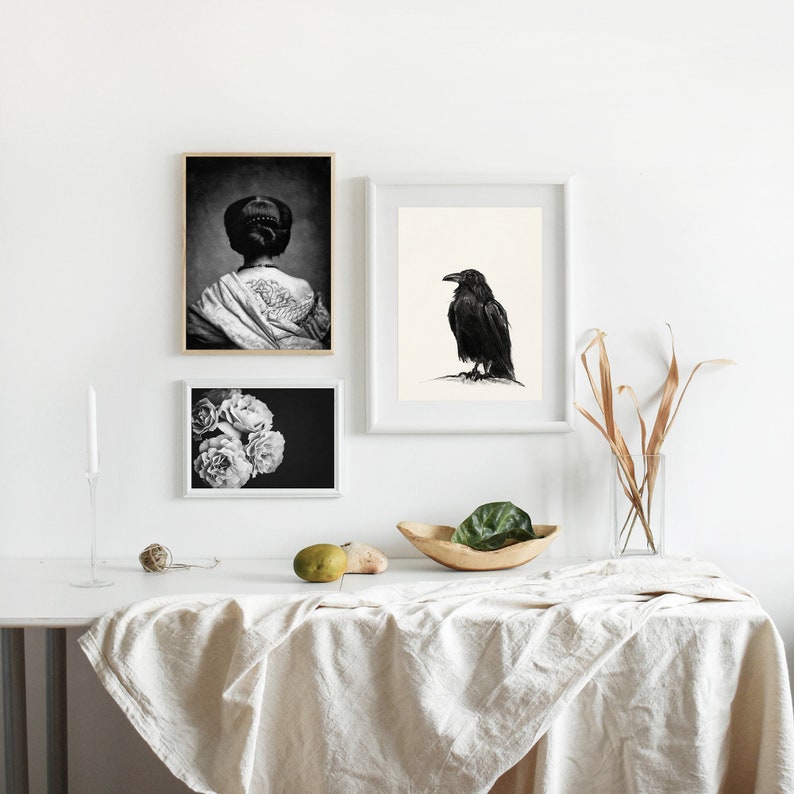 May include: Three black and white framed prints on a white wall. The prints are of a woman with a tattoo, a raven, and a bouquet of flowers.