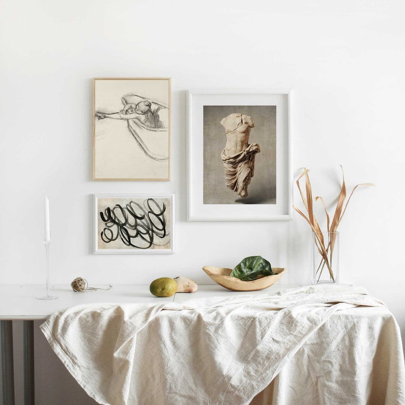 Pu&ograve; includere: Tre stampe incorniciate su una parete bianca sopra un tavolo bianco con una tovaglia di lino. Le stampe sono di un design astratto in bianco e nero, un disegno in bianco e nero di una persona in una vasca da bagno e una fotografia a colori di una statua di marmo di una persona.