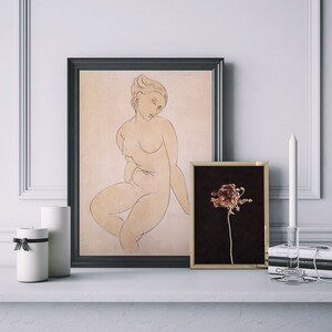 May include: Two framed prints on a white shelf. The print on the left is a line drawing of a nude woman in a seated pose. The print on the right is a black and white photograph of a dried flower.