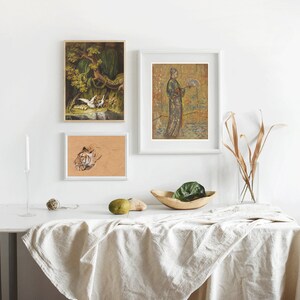 May include: Three framed prints on a white wall above a white table with a linen tablecloth. The prints are of a tiger, a woman in a kimono, and a bird in a tree.