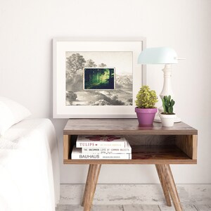 Puede incluir: Una imagen enmarcada en blanco con una imagen de paisaje en blanco y negro con una escena de bosque verde dentro de un marco m&aacute;s peque&ntilde;o. La imagen est&aacute; sobre una mesa auxiliar de madera con dos libros apilados uno encima del otro. Los libros se titulan "Tulips" y "The Uncommon Life of Common Objects". Una l&aacute;mpara con una pantalla azul claro est&aacute; sobre la mesa junto a la imagen.