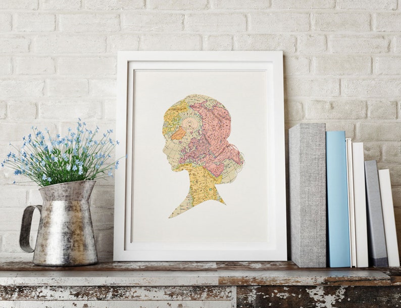 May include: A white framed print of a silhouette of a person's head with a vintage map design. The map is in shades of pink, yellow, and blue.
