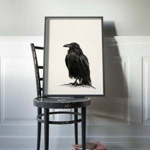 May include: A black and white drawing of a crow in a black frame, hanging on a white wall above a black wooden chair.