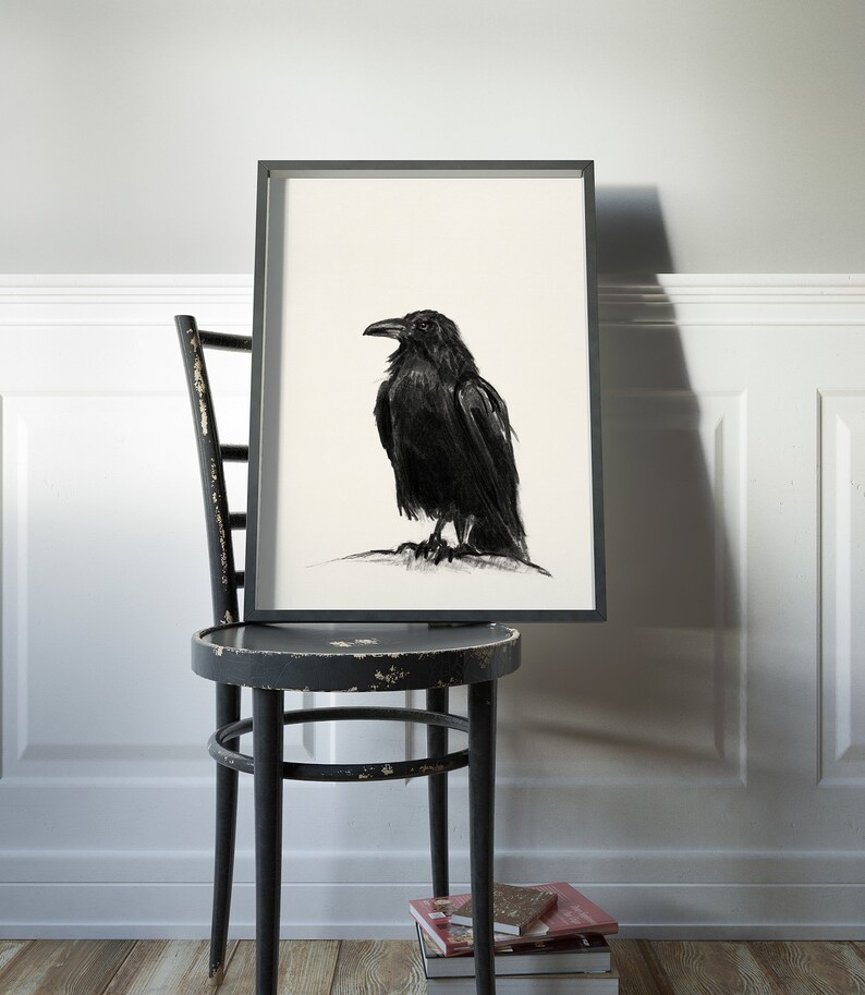 May include: A black and white drawing of a crow in a black frame, hanging on a white wall above a black wooden chair.