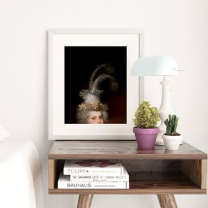 May include: A framed art print depicting a person in a feathered headdress and jewelry. The print is on a wooden bedside table with a lamp, plants, and books. The color scheme includes black, white, and gold, creating a classic aesthetic.