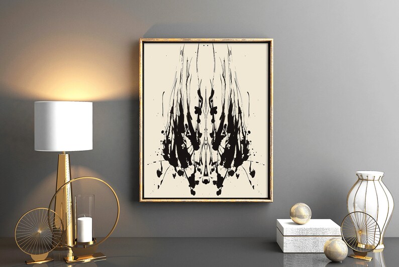 May include: A black and white abstract art print in a gold frame, hanging on a gray wall above a gold metal decorative stand with a candle and two circular metal accents. The stand is on a black surface.