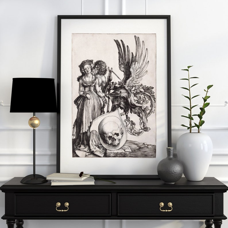 May include: A black and white print of a woman and a man with a skull and a winged creature. The print is framed in a black frame and is hanging on a white wall.