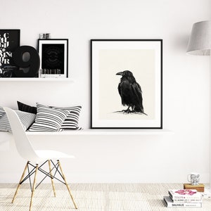 May include: A black and white illustration of a raven perched on a branch, framed in a black frame, hanging on a white wall. The wall is decorated with other black and white framed artwork and a black number nine.