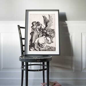 May include: Black and white print of a Renaissance-era engraving depicting a couple standing next to a skull and a winged creature. The print is framed in a black frame and is hanging on a wall.