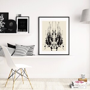 May include: A black and white abstract art print in a black frame hangs on a white wall above a white shelf with black and white striped pillows. A white chair with wooden legs sits in front of the shelf. A white lamp with a gray shade stands in the corner of the room.