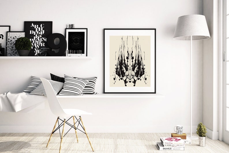 May include: A black and white abstract art print in a black frame hangs on a white wall above a white shelf with black and white striped pillows. A white chair with wooden legs sits in front of the shelf. A white lamp with a gray shade stands in the corner of the room.