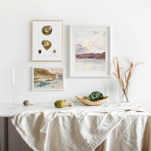 May include: Three framed prints on a white wall, a white table with a linen tablecloth, a wooden bowl with a green plant, and a vase with dried branches. The prints are of a seascape, a seashell, and a boat.