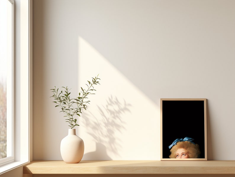 Pu&ograve; includere: Un vaso bianco con una pianta verde si trova su uno scaffale di legno accanto a un quadro incorniciato di una donna con un nastro blu nei capelli. L'immagine &egrave; su uno sfondo nero.