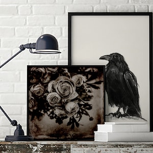 May include: A black and white photograph of a bouquet of roses with a black raven in a black frame on a white brick wall.