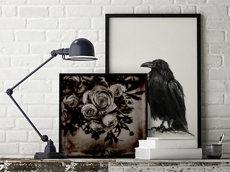 May include: A black and white photograph of a bouquet of roses with a black raven in a black frame on a white brick wall.