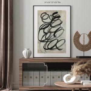 May include: A framed abstract art print with black brushstrokes on a beige background. The print is displayed on a wooden shelf with a white vase and a decorative wooden piece.