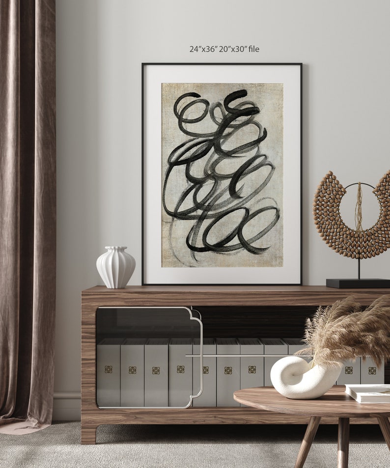 May include: A framed abstract art print with black brushstrokes on a beige background. The print is displayed on a wooden shelf with a white vase and a decorative wooden piece.