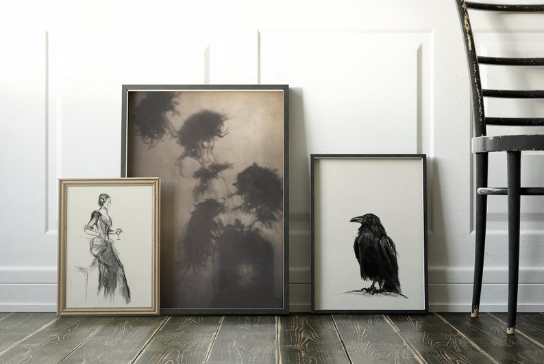 May include: Three framed black and white drawings on a wooden floor. The drawing on the left is of a woman in a long dress holding a glass. The middle drawing is of a misty forest scene. The drawing on the right is of a black raven.
