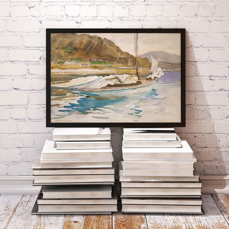 May include: A framed watercolor painting of a sailboat with white sails on a body of water. The boat is anchored in the water with mountains in the background. The painting is on a white brick wall with a stack of books on either side.