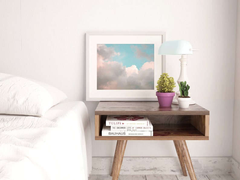 May include: A white bedside table with a wooden top and legs. There are three books stacked on the table, with the top book titled "Tulips: An Ever-Present Family". A small potted plant and a lamp are on the table.