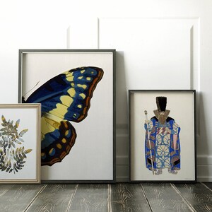 May include: Three framed prints on a wooden floor. The leftmost print features a collage of green leaves. The center print features a blue and yellow butterfly wing. The rightmost print features a man in a blue and gold patterned robe holding a staff.