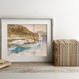 May include: A framed watercolor painting of a sailboat with white sails on a body of water. The boat is anchored near a rocky shore with green trees and a mountain in the background. The water is a light blue with reflections of the sky and the boat.