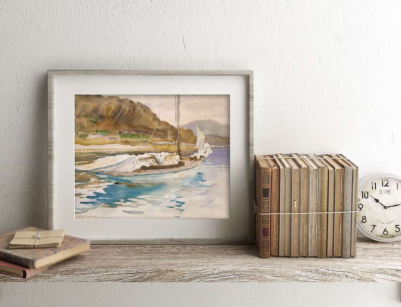 May include: A framed watercolor painting of a sailboat with white sails on a body of water. The boat is anchored near a rocky shore with green trees and a mountain in the background. The water is a light blue with reflections of the sky and the boat.