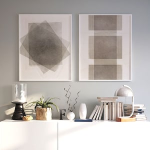 Pu&ograve; includere: Due stampe artistiche astratte incorniciate con disegni geometrici sono appese sopra un mobile bianco. Il mobile espone un portacandele nero, una pianta in vaso, oggetti decorativi, libri e una lampada moderna. L'arte e l'arredamento creano un'estetica minimalista.