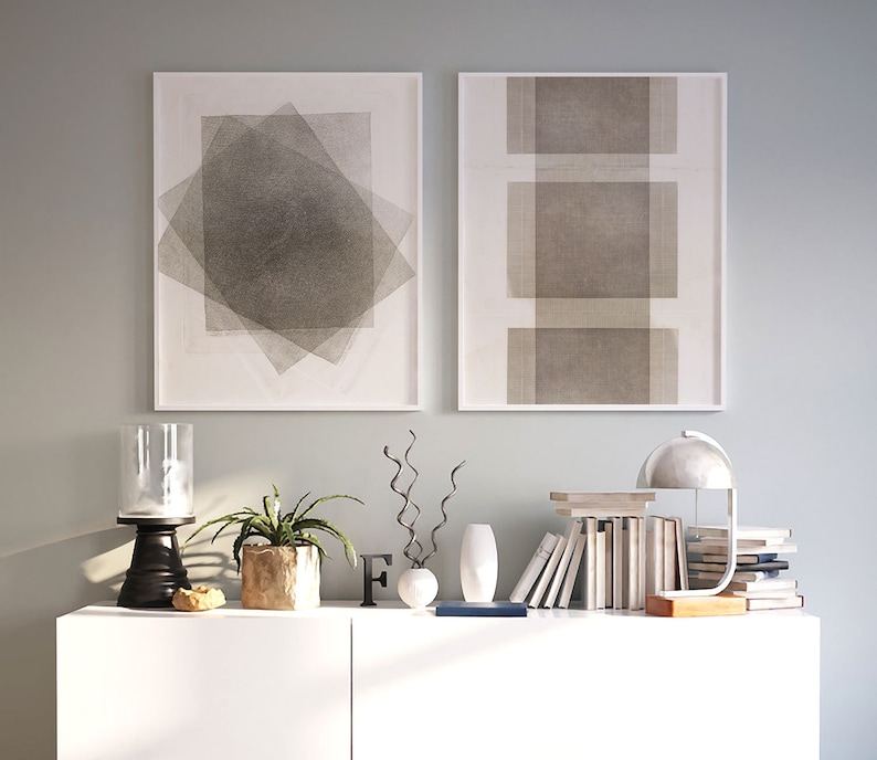 Pu&ograve; includere: Due stampe artistiche astratte incorniciate con disegni geometrici sono appese sopra un mobile bianco. Il mobile espone un portacandele nero, una pianta in vaso, oggetti decorativi, libri e una lampada moderna. L'arte e l'arredamento creano un'estetica minimalista.
