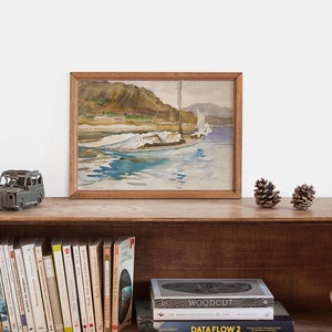 May include: A framed watercolor painting of a sailboat with white sails on a body of water. The painting is on a wooden shelf with a small toy car and pine cones in front of it. There are books on the shelf below the painting.