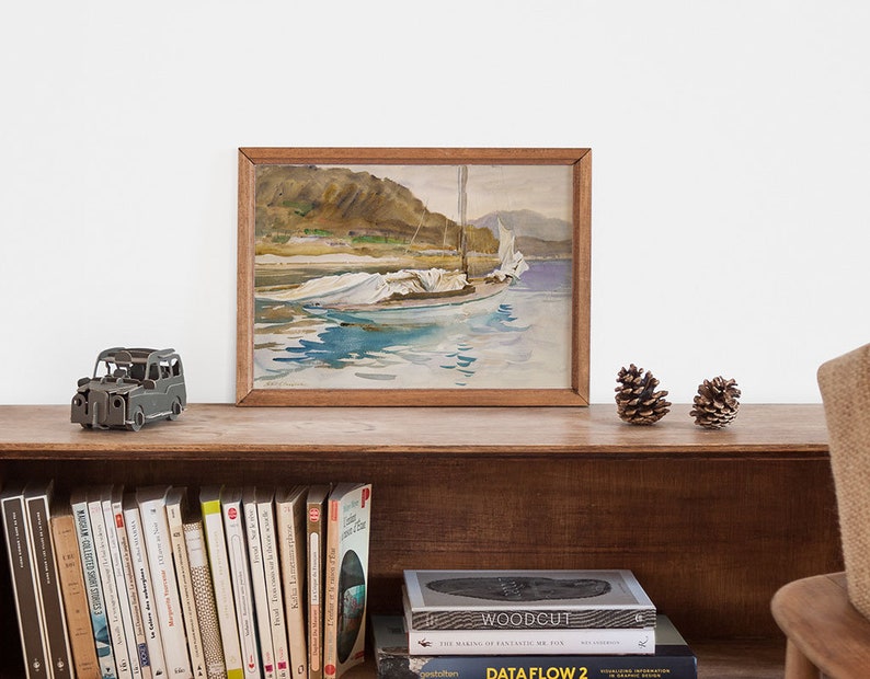May include: A framed watercolor painting of a sailboat with white sails on a body of water. The painting is on a wooden shelf with a small toy car and pine cones in front of it. There are books on the shelf below the painting.