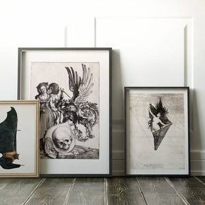 May include: Three framed black and white prints on a white wall with a black wooden chair in the corner. The prints are of a bat, a couple with a skull and a woman in a spider web.