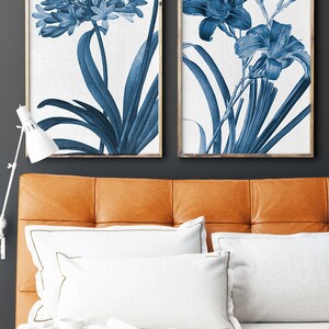 May include: Two framed prints of blue botanical illustrations. The prints feature detailed drawings of flowers and leaves in a blue and white color scheme. The prints are framed in a simple wooden frame.