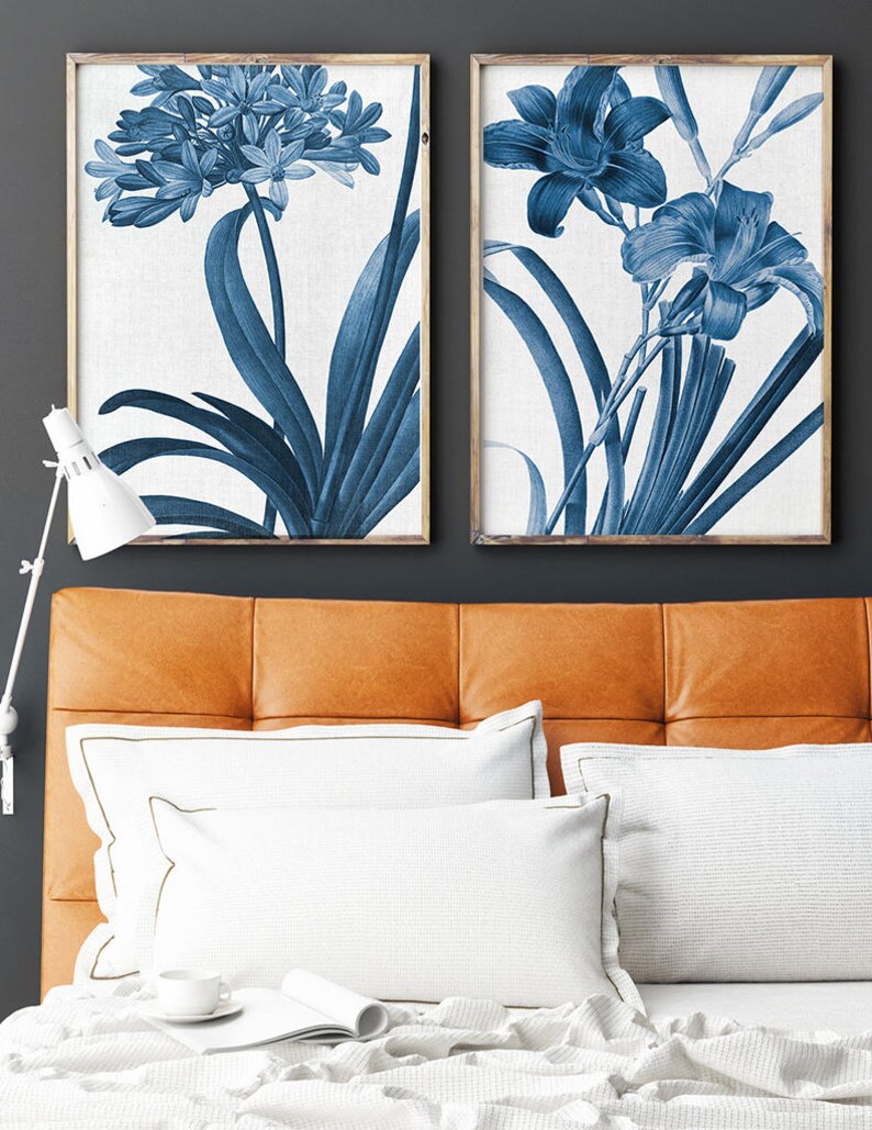 May include: Two framed prints of blue botanical illustrations. The prints feature detailed drawings of flowers and leaves in a blue and white color scheme. The prints are framed in a simple wooden frame.