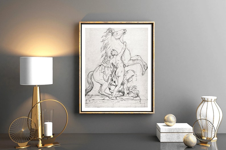 May include: A black and white framed print of a drawing of a man struggling with a rearing horse. The print is hanging on a gray wall above a gold metal table lamp and decorative candle holder.