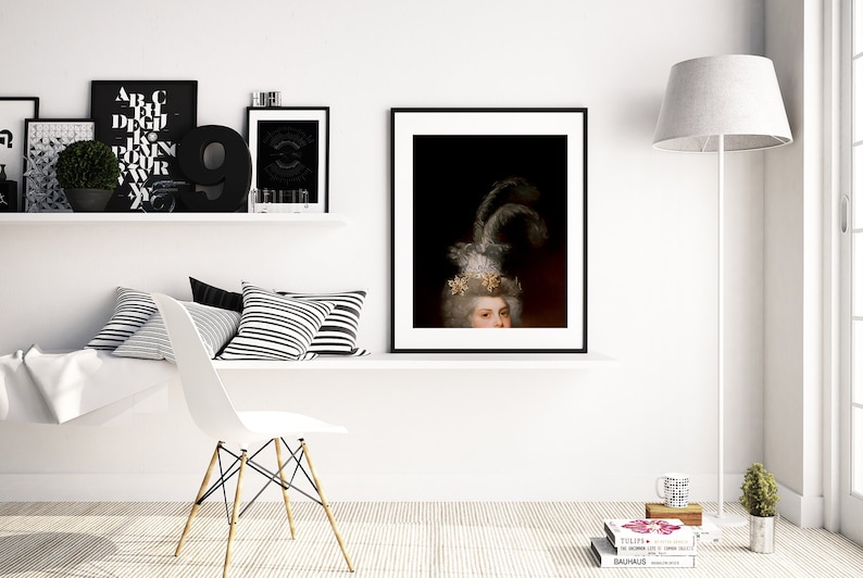 May include: A framed portrait of a person with a white wig and ornate headpiece, featuring feathers and gold accents. The artwork is displayed on a white wall, alongside other framed art and decorative items, creating a sophisticated interior design.