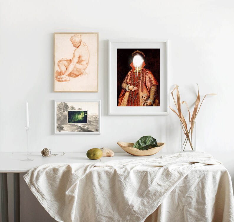 Puede incluir: Tres cuadros enmarcados en una pared blanca sobre una mesa blanca con un mantel blanco. Los cuadros son de un dibujo de un hombre desnudo, una pintura de una persona con una t&uacute;nica roja y la cara blanca, y una escena de paisaje.