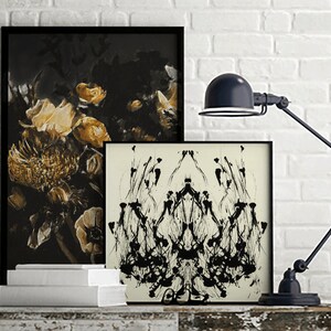 K&ouml;nnte beinhalten: Zwei gerahmte Schwarzwei&szlig;-Abstraktkunst-Drucke mit einer schwarzen Schreibtischlampe vor einem wei&szlig;en Backsteinwand-Hintergrund.